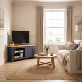 [Blue] A styled living room interior featuring a corner navy blue TV stand with a light wood top, a beige sofa, a round wooden coffee table, and a large woven jute rug