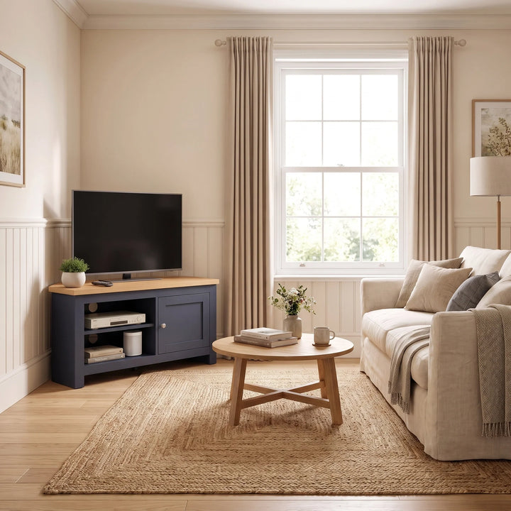 [Blue] A styled living room interior featuring a corner navy blue TV stand with a light wood top, a beige sofa, a round wooden coffee table, and a large woven jute rug