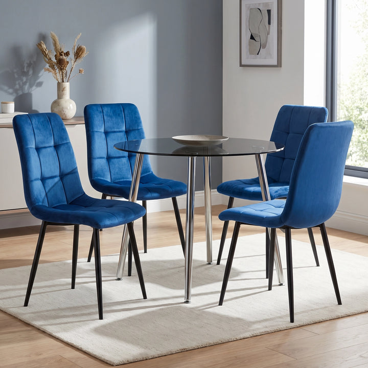 [Blue | Set of 4] Velvet dining chairs around a round black table, with curved tufted backs, padded seats and black legs.