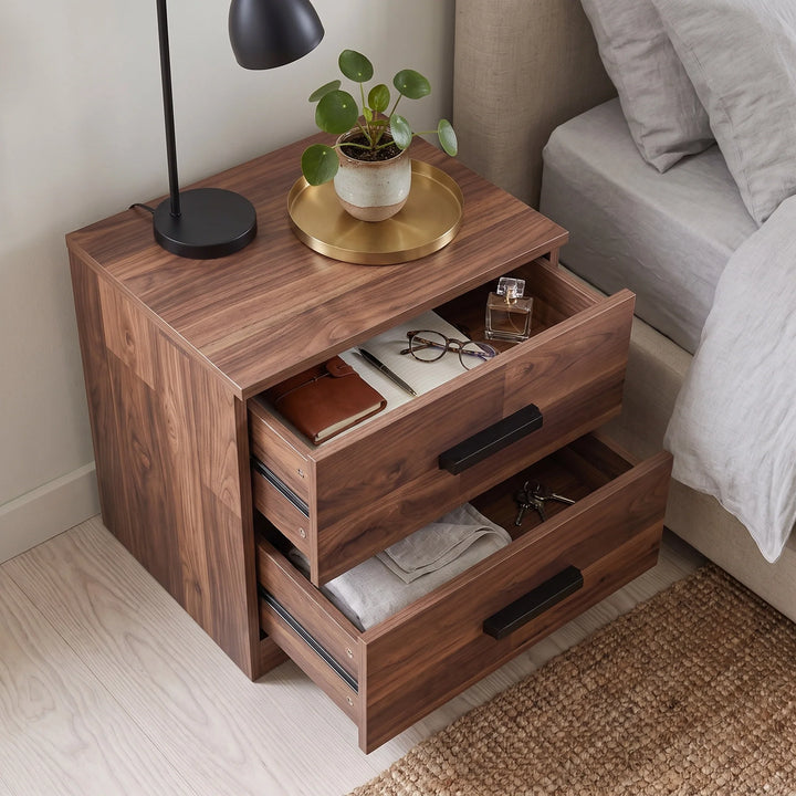 [Dark Bronx] nightstand with three drawers, shown in a bedroom setting next to a bed. The top drawer is open, displaying books, a notebook, and a small bottle, while the bottom drawer is partially pulled out.