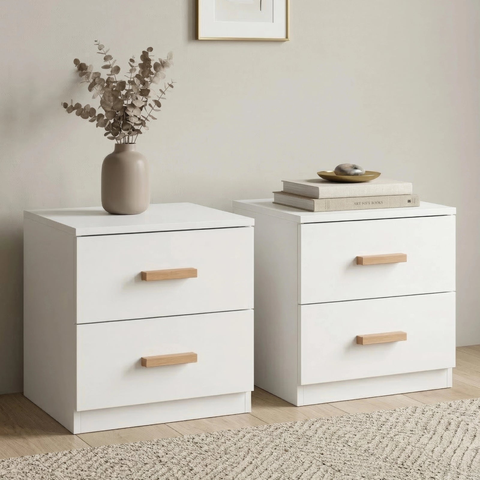 [White] Front three quarter view of two white bedside tables on woven rug with dried stems in vase and books on top