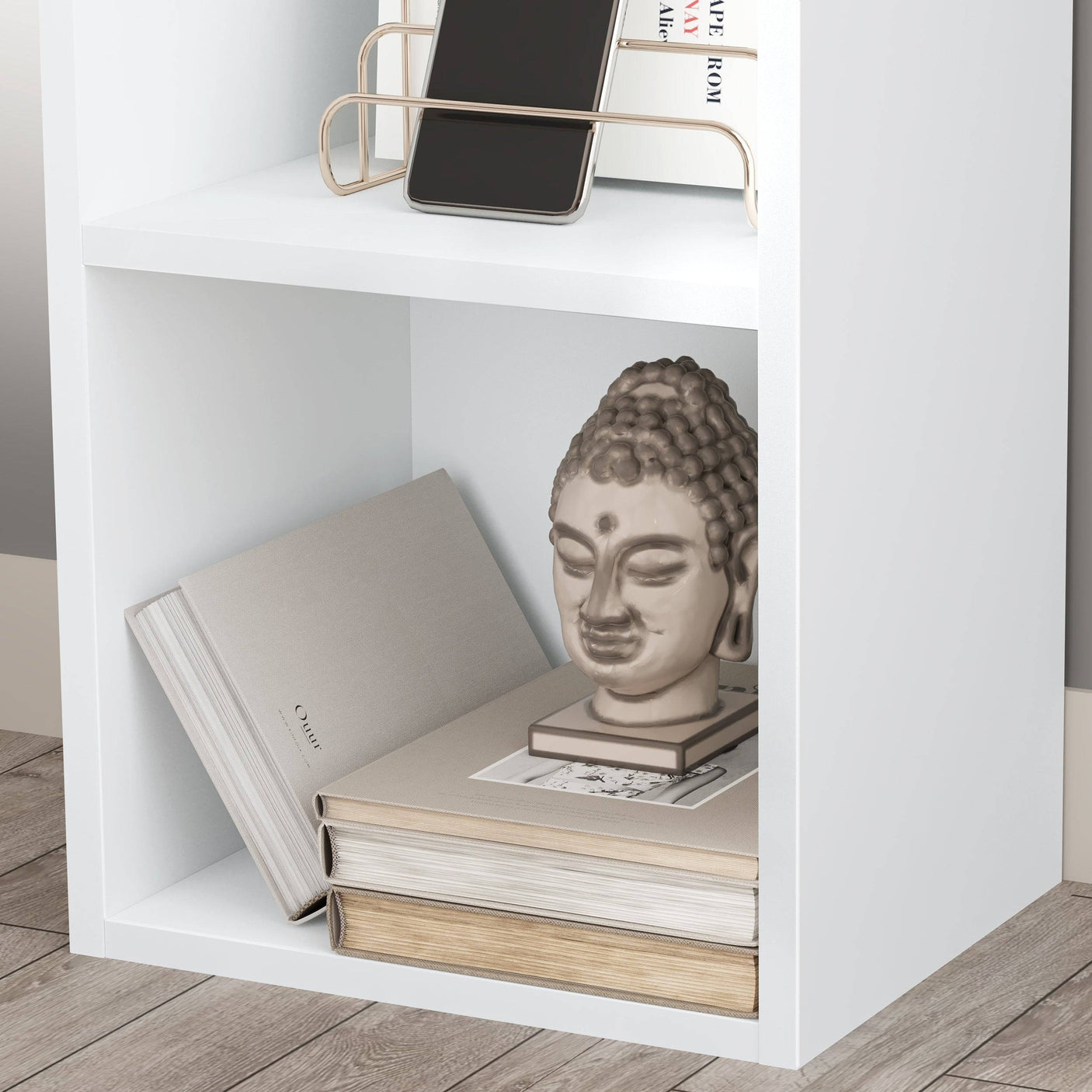 Close-up of lower shelf on Blisswood white bookcase, styled with books and decorative Buddha head.