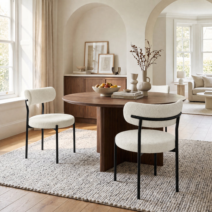 [Cream | Set of 4] Two boucle dining chairs beside a round wooden table in a bright open-plan room.