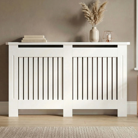 [Large] Chelsea White Radiator Cover front-facing in taupe room on wooden floor with pampas vase, stacked books, and rose gold lantern on wide dual-panel top