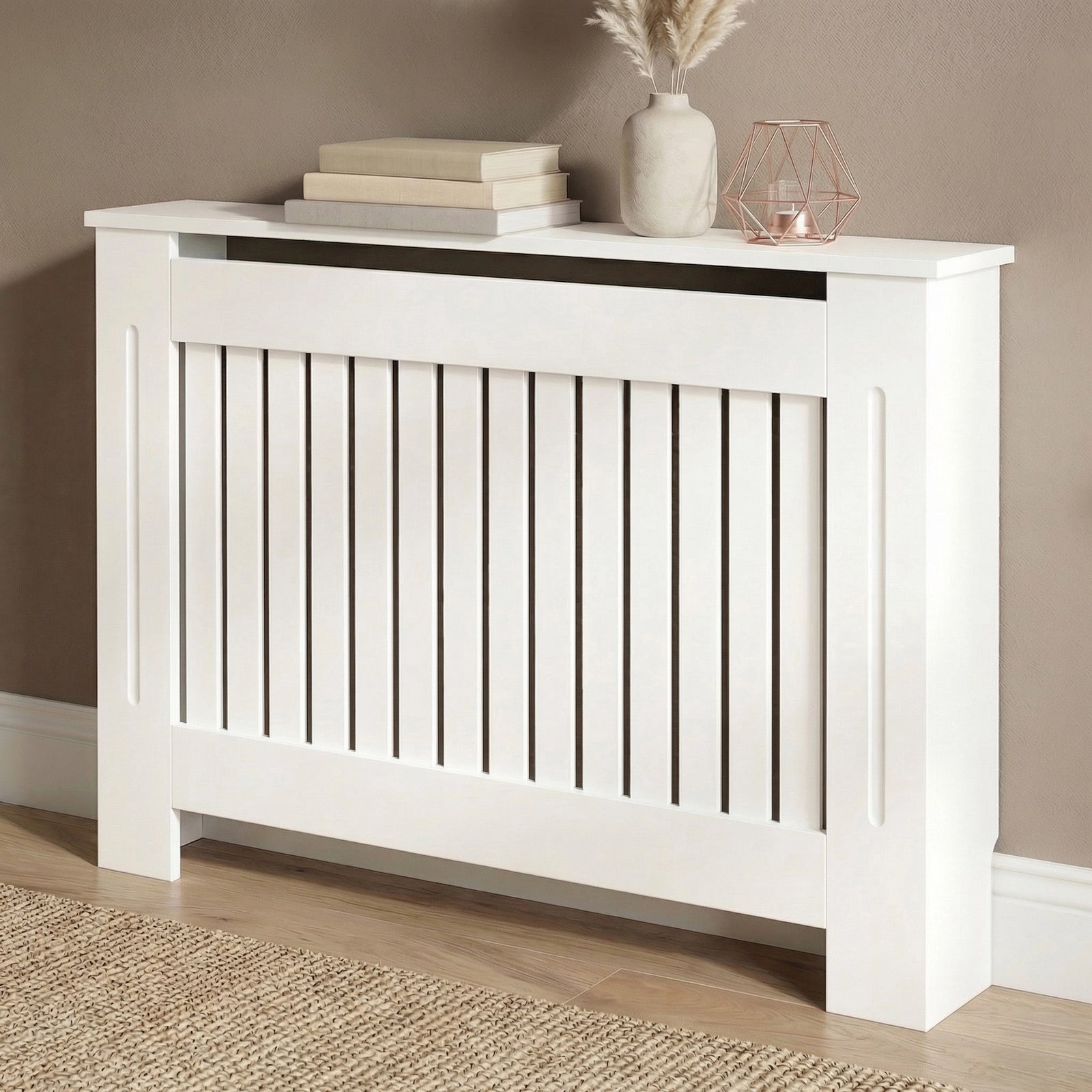 [Medium] Chelsea White Radiator Cover angled three-quarter view in taupe room on wooden floor with jute rug and rose gold accessories on top shelf