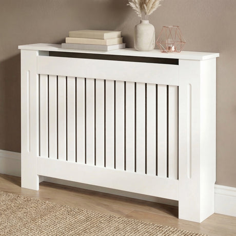 [Medium] Chelsea White Radiator Cover angled three-quarter view in taupe room on wooden floor with jute rug and rose gold accessories on top shelf