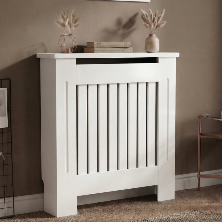 [Small] Chelsea White Radiator Cover angled three-quarter view in taupe room with two pampas vases on top and wire grid wall panel alongside