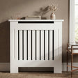 [Small] Chelsea White Radiator Cover front-facing in warm taupe room with rose gold lantern, stacked books, and pampas grass vase on top shelf