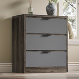 Chest of 3 drawers in a wooden grey finish with decorative items on top, placed in a bright setting near a window