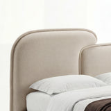 Soft beige fabric headboard with a gently curved top edge, placed with white pillows and layered bedding