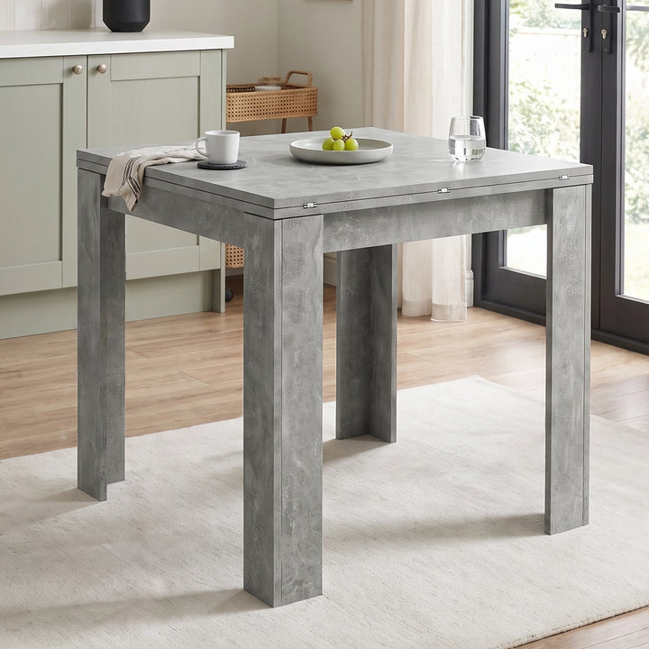 [Concrete] Closed square flip-top dining table styled with a mug, fruit bowl and glass in a bright kitchen.