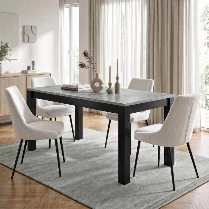 [140cm | Concrete] Closed table in bright dining room with four cream chairs, vases, candles, rug, and window light