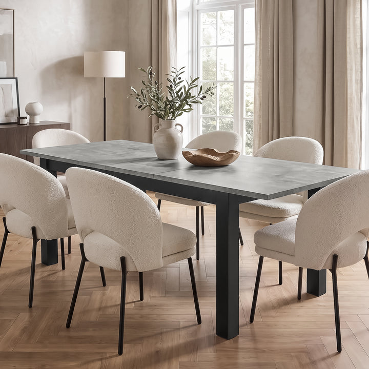 [160 cm | Concrete] Extended 200cm dining table with six cream chairs, leafy vase and wooden bowl in a bright dining room.
