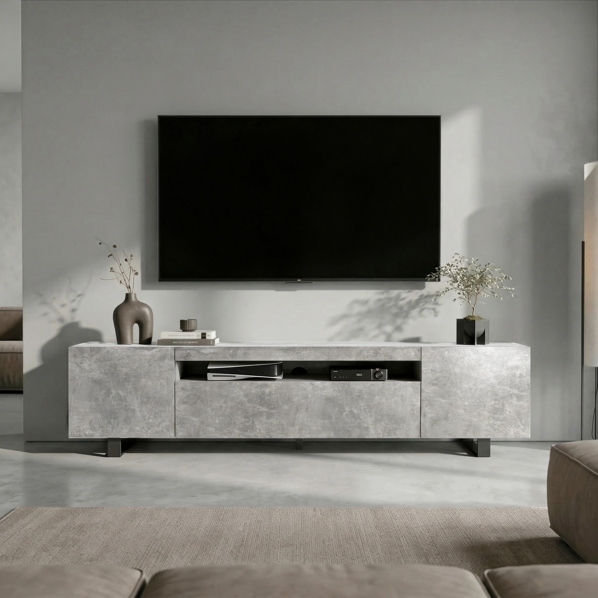 [Concrete] Kystra TV stand front-facing view in a grey living room with a large wall-mounted TV, closed concrete-effect cabinets either side and open centre shelf with AV equipment