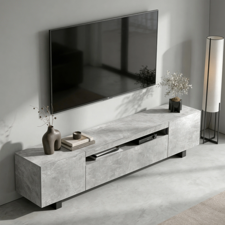 [Concrete] Kystra TV stand viewed from above at an angle in a minimal living room, showing the concrete-effect top surface, open centre shelf with AV unit, dark vase on the left, and floor lamp to the right
