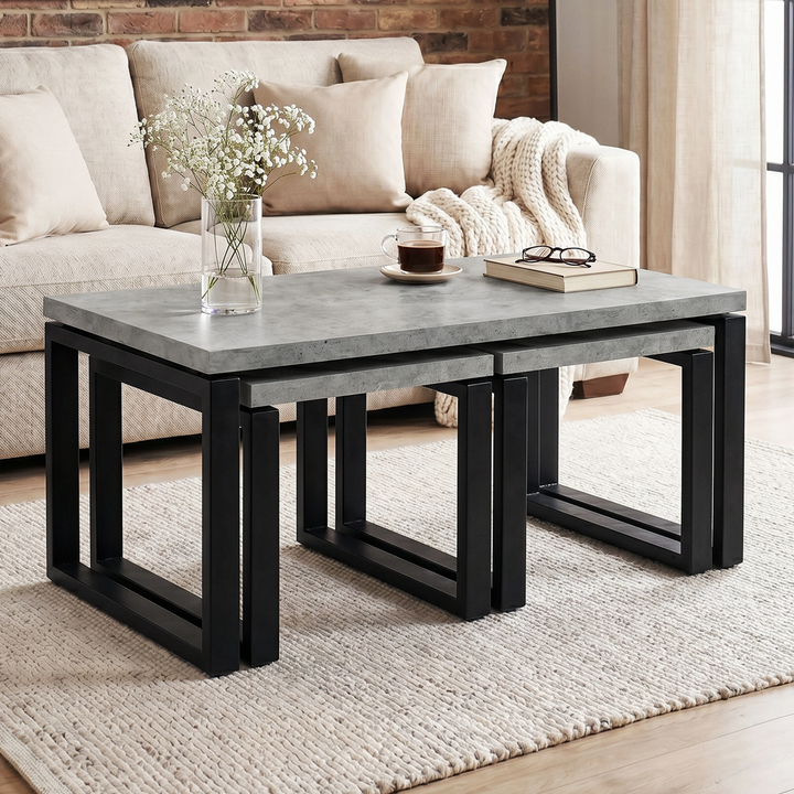 [Concrete] Nestline nesting table view showing in a bright lounge with cream sofa, brick wall, vase stems, and nested frames