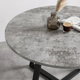 [Concrete] Close-up of the round concrete-effect tabletop with mottled patterning, styled with a vase, coffee and paper.