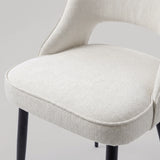 [Cream | Set of 4] Comfy dining chair close-up view of woven seat, piped edge, curved open back & black metal legs.