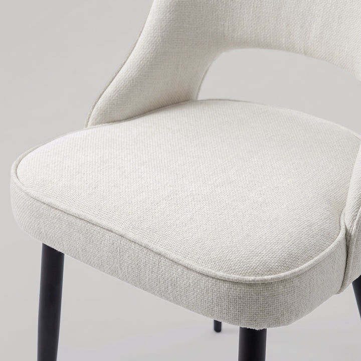 [Cream | Set of 4] Comfy dining chair close-up view of woven seat, piped edge, curved open back & black metal legs.