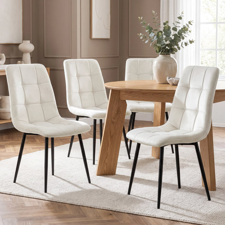 [Cream | Set of 4] Velvet dining chairs around a rectangular wood-effect table, showing curved tufted backs and slim black metal legs.
