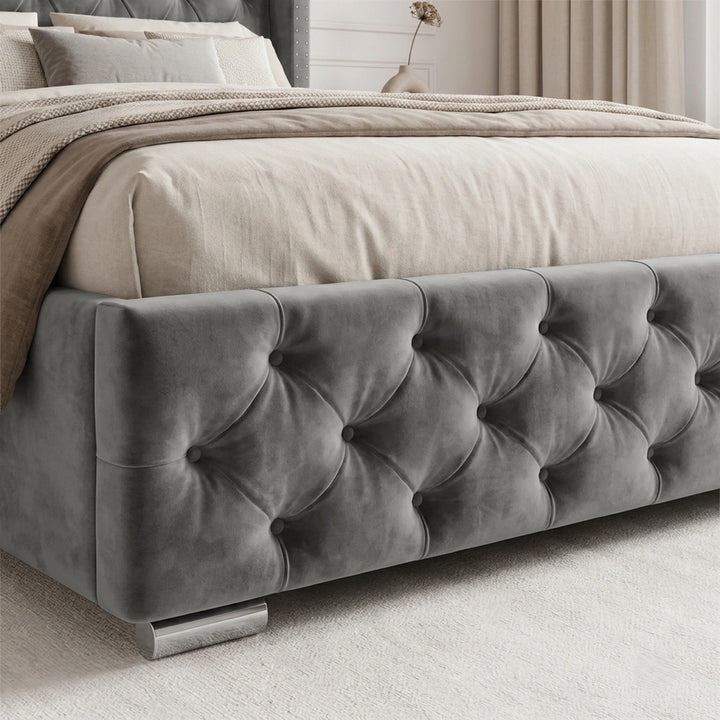 [Small Double | Grey] bed frame upholstered in dark gray tufted velvet, shown with beige bedding and a neutral blanket in a softly lit bedroom setting.