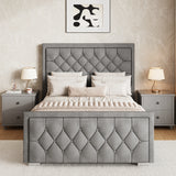 Grey upholstered ottoman bed king with a matching cross-puffed headboard and footboard placed between two bedside tables.