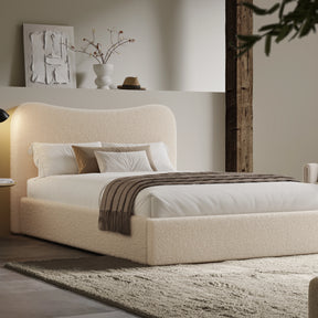 [King | Beige] Boucle fabric ottoman bed from the side with white bedding and fringed throw beside floating shelf with art