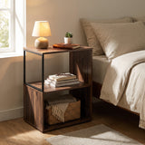 [Dark Bronx] This narrow side table stands beside a bed with a lamp, books and a basket on its open shelves.