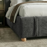 Lower corner detail of upholstered base of double bed frame with rounded edges and light wooden feet