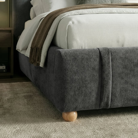 Lower corner detail of upholstered base of double bed frame with rounded edges and light wooden feet