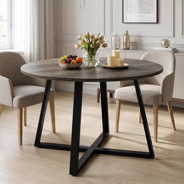[Dark Wood] Round dining table in a bright room with flowers, fruit and candles on top, set between beige chairs.