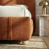 Rounded upholstered foot section with vertical strip stitching and wood support leg placed on a rug