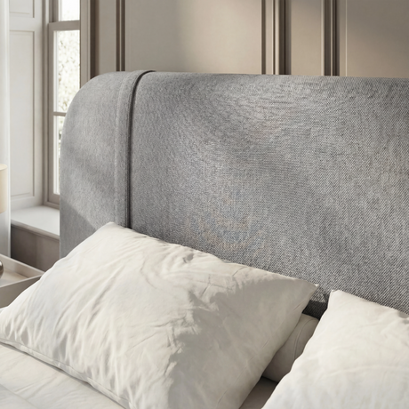 Close detail of curved padded headboard in textured grey fabric upholstery in a natural light space
