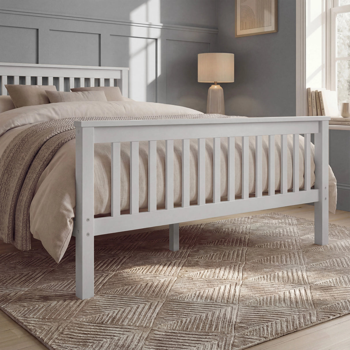 White double bed frame with slatted rails, neutral bedding, and a rug placed beneath in a natural light room
