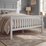 White double bed frame with slatted rails, neutral bedding, and a rug placed beneath in a natural light room