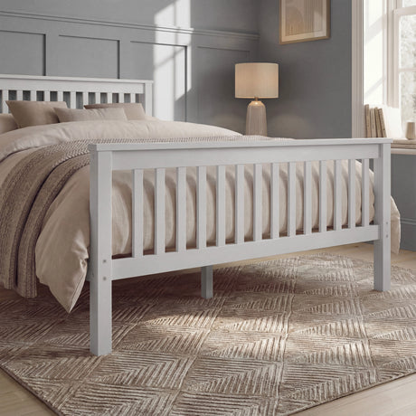 White double bed frame with slatted rails, neutral bedding, and a rug placed beneath in a natural light room