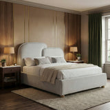 Upholstered double bed in grey fabric positioned near a window with layered bedding and bedside lighting