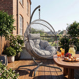 [Grey] Hanging chair on a wooden deck with a table of snacks and drinks, surrounded by plants and a building in the background