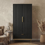 Black freestanding wardrobe in flutrina design with gold handles and legs placed in a natural light room