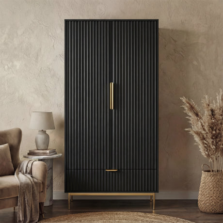 Black freestanding wardrobe in flutrina design with gold handles and legs placed in a natural light room