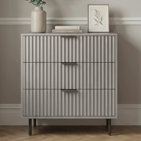 Grey Flutrina 3 drawer chest with panels and brushed black metal handles placed in a natural light room