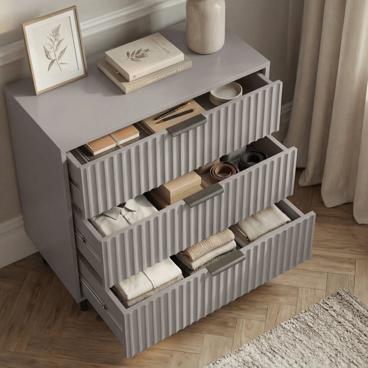 Grey chest of drawers opened to reveal internal storage layout across three levels with black metal handles