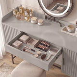 Grey vanity dressing table with a round mirror and an open drawer containing beauty products and accessories