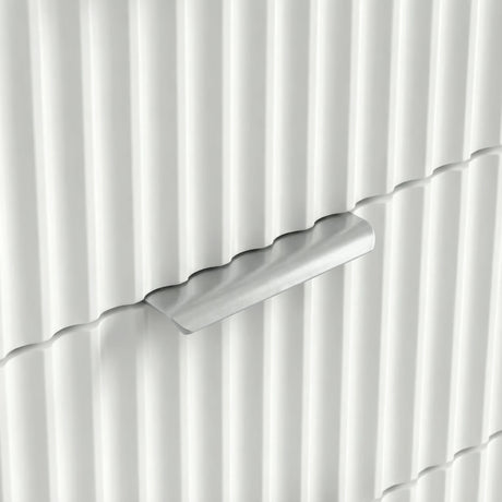 Close view of silver metal handle on white flutrina front of chest of drawers in a natural light 