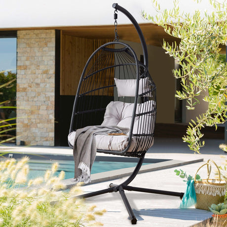 [Black] Black foldable garden egg chair with cushion on patio, pool and stone wall behind