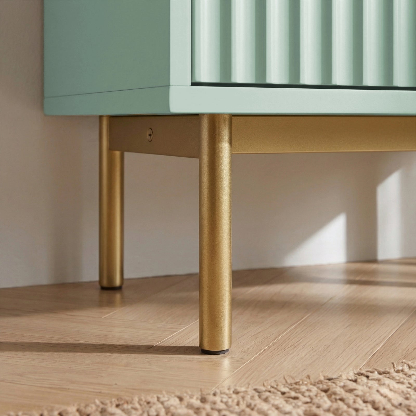 [Green] Flutrina shoe cabinet foot detail, two gold legs lifting ribbed sage cabinet over light wood planks