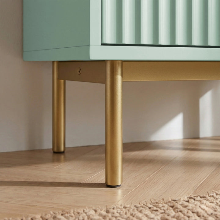 [Green] Flutrina shoe cabinet foot detail, two gold legs lifting ribbed sage cabinet over light wood planks