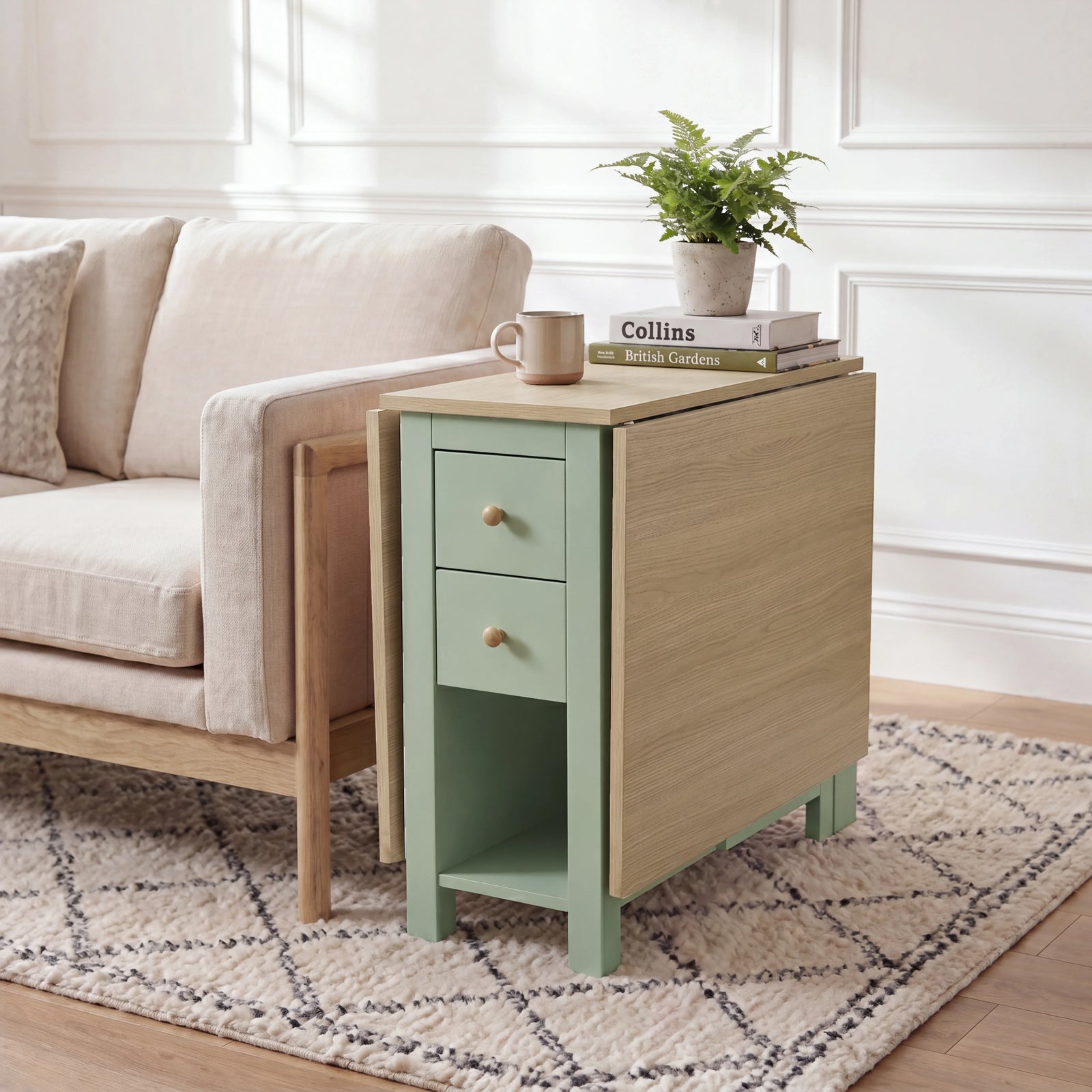 [Green] Stovra Drop Leaf Dining Table used as a side table beside a sofa with one leaf extended and plant on top