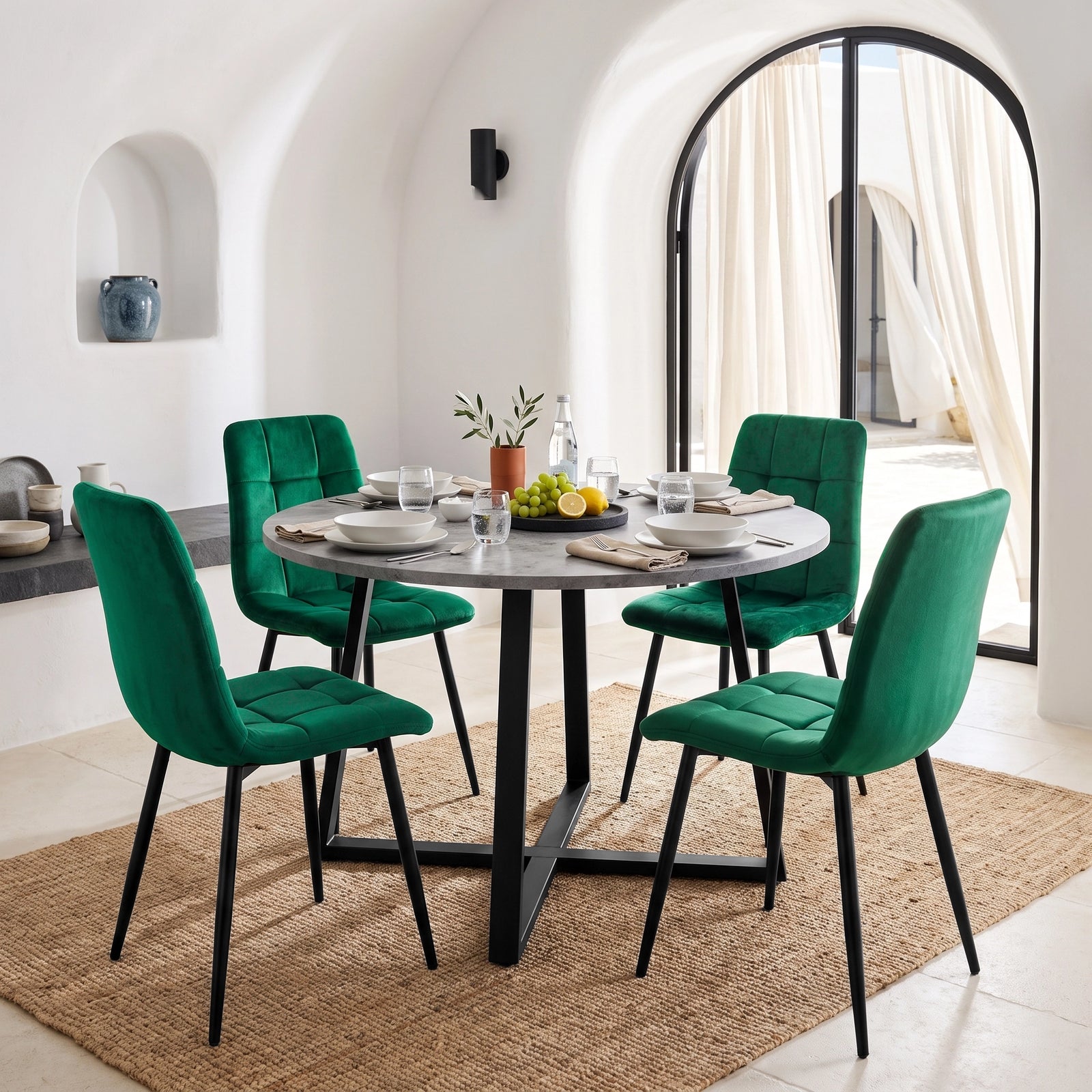 [Green | Set of 4] Velvet dining chairs around a round grey table, with curved tufted backs, armless seats and black legs.