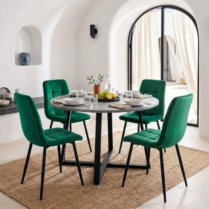 [Green | Set of 4] Velvet dining chairs around a round grey table, with curved tufted backs, armless seats and black legs.